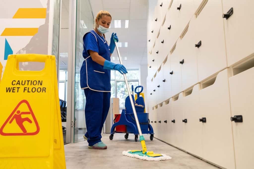 A cleaner with a mask on her face cleans the floor with the mop.